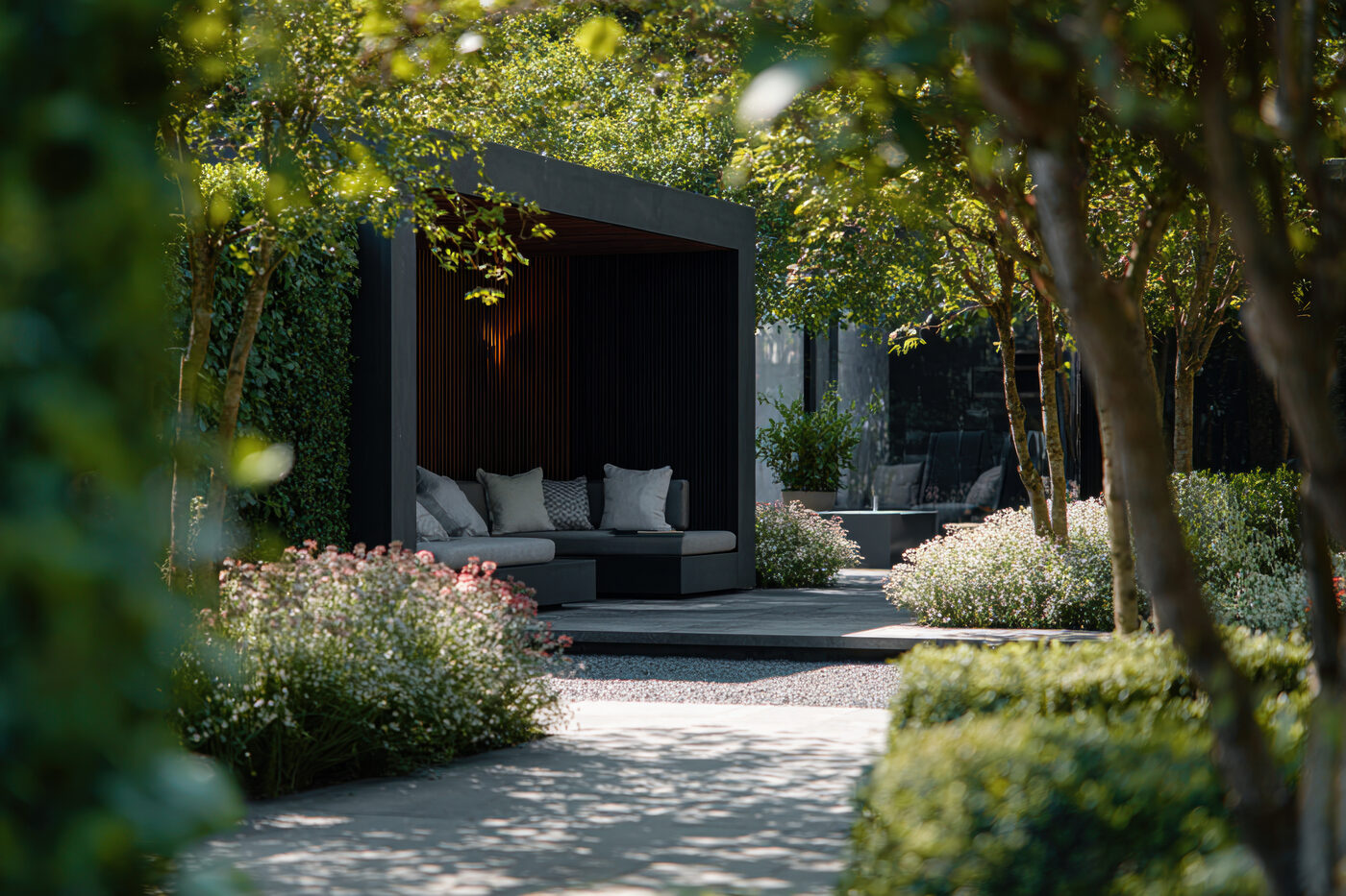 Dark modern outdoor pavilion with built-in seating in a landscaped garden at dusk